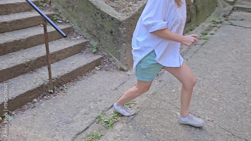 Woman is sitting on a set of stairs and riding on railings. The stairs are made of concrete and are located on a hill. Father is waiting down