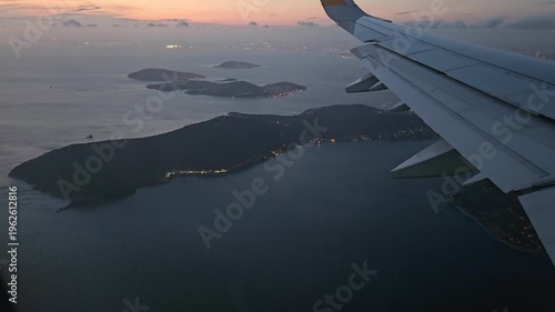 Plane is flying over the ocean with a beautiful sunset in the background. The sky is filled with clouds and the water is calm