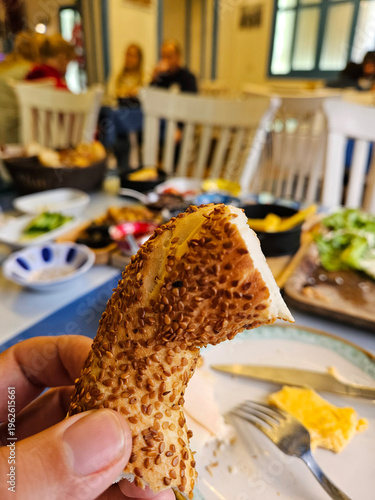 Wallpaper Mural Person is holding a piece of bread with sesame seeds on it. The bread is cut in half and is on a plate. There are other plates and bowls on the table, and a fork and knife are also present Torontodigital.ca