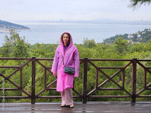 Wallpaper Mural Woman in a pink raincoat stands on a wooden deck overlooking a body of water. She is holding a black purse and she is enjoying the view Torontodigital.ca