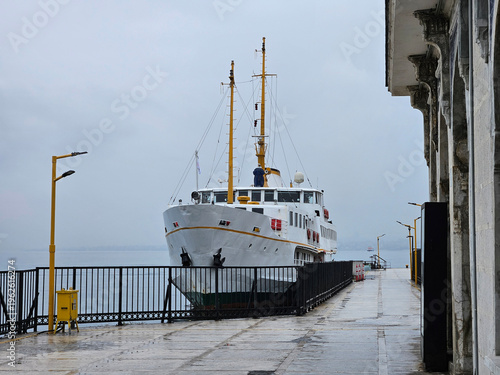 Wallpaper Mural Large white boat is docked at the pier. The boat is surrounded by a yellow fence. The sky is cloudy and the water is calm Torontodigital.ca