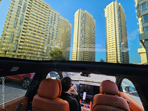 Wallpaper Mural MOSCOW - SEP 30 , 2025: Man is driving a car with a view of tall buildings in the background. The car is parked in a lot with several other cars Torontodigital.ca