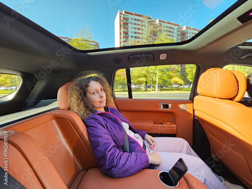 Wallpaper Mural Woman is sitting in the back seat of a car with a phone in her hand. The car is parked in front of a building Torontodigital.ca