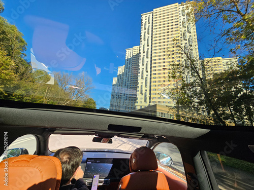 MOSCOW - SEP 30, 2025: Man is sitting in a car with a view of a tall building. The car is parked on a street with trees in the background