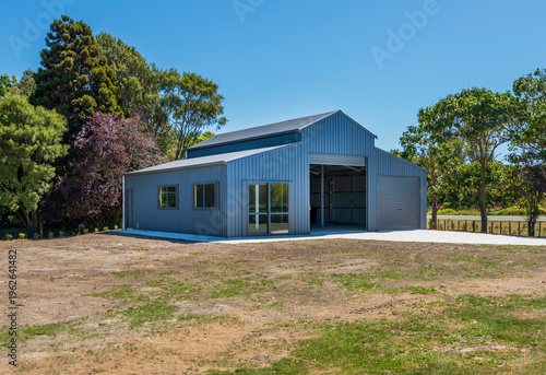  modern blue coloured steel frame building set on a dry grassy lawn with trees and blue sky frame the structure