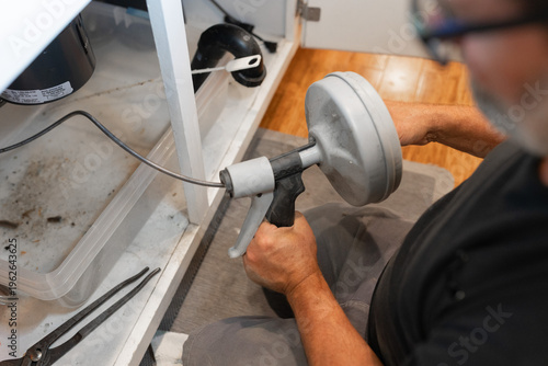 Photos A plumber uses a drain snake, or auger, to clear a blockage from a pipe, water s