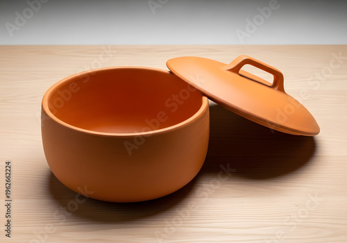 Terracotta cooking pot with lid resting on a wooden surface. Empty pot in a neutral studio setting. Kitchenware for a home cook. modern style. studio shot.