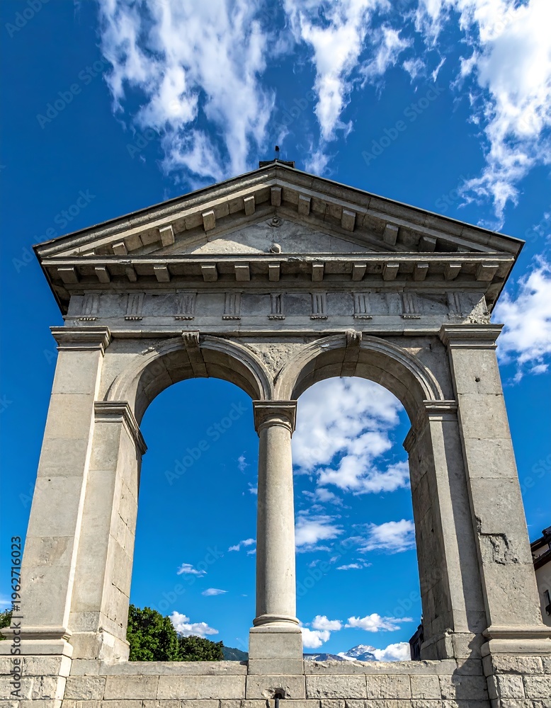 Obraz premium Ancient stone archway with two openings under bright blue sky, puffy clouds, and mountains