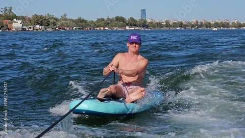 Man is sitting on a surfboard in the ocean. He is wearing a purple bandana and is holding a surfboard leash