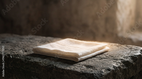 Folded white linen cloth on stone inside empty tomb, Easter morning resurrection of Jesus Christ, biblical burial shroud concept