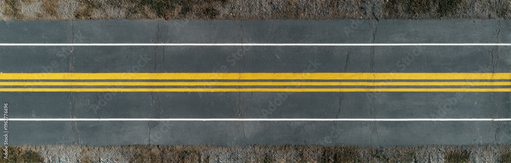 Fototapeta premium Bird's-eye view of an empty asphalt road featuring yellow double center lines and textured dark gray surface with subtle wear marks