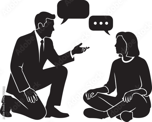 A professional man in a suit kneeling down to have a conversation with a seated woman in a relaxed posture while both engage in dialogue