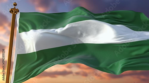A green and white striped flag waves against a cloudy sky at sunset