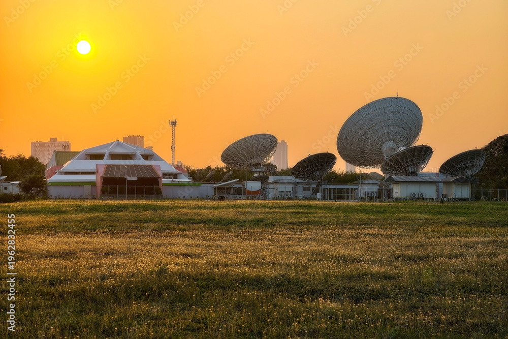 Obraz premium Large satellite dish antenna station by meadow at sunset, Bangkok