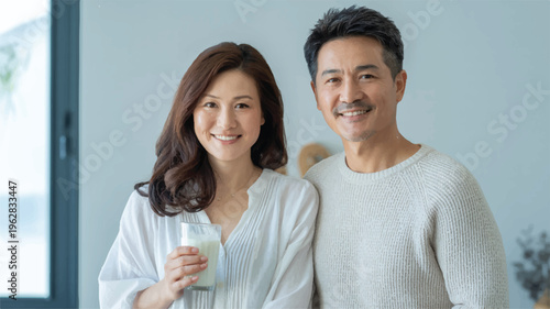 Asian senior couple smiling and holding milk in modern kitchen