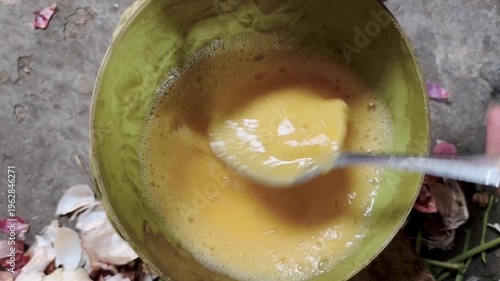 Whisked eggs in a light green bowl, with a spoon stirring the mixture.