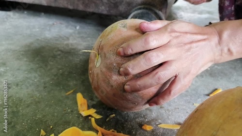 Hands peeling a large pumpkin with a knife, with discarded peelings scattered on the floor.