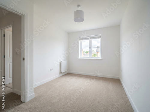 An empty room with white walls and a window showing a view of another house outside.