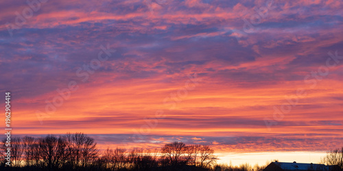 Vibrant sunset sky with layered colorful clouds over rural tree silhouettes