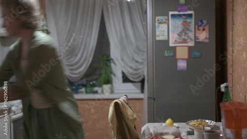 A young woman is cooking dinner in the kitchen, moving energetically and positively, in a happy mood.
