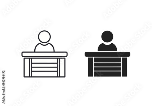 Two people sit at desks in a meeting or discussion setting indoors