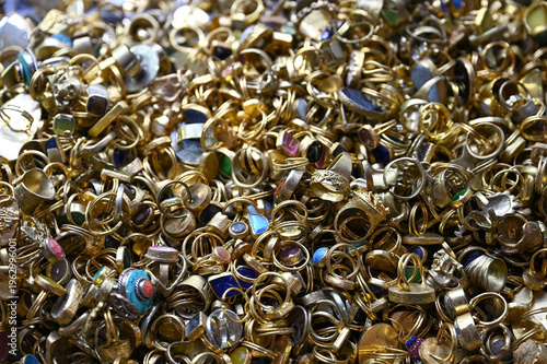 A dense and jumbled heap of gold-toned rings, many set with various colorful gemstones