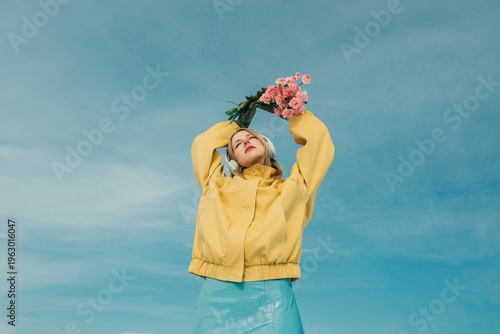 Woman in yellow jacket enjoying music with flowers