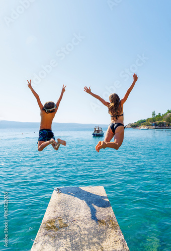 Canvas Print Siblings jumping into turquoise sea from a pier in Croatia