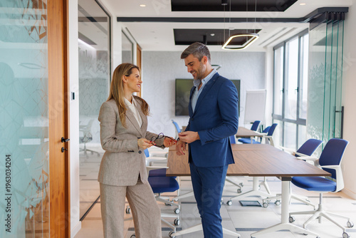 Photos Two business professionals in business attire stand and conversing in a bright,