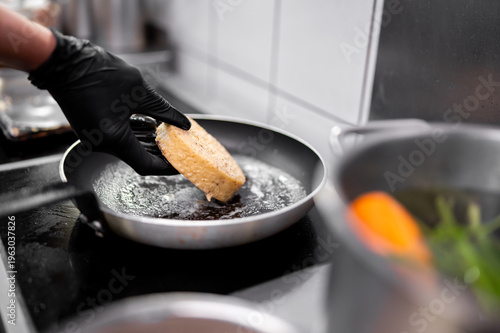 Valokuva Close-up of a chef in black gloves frying a thick slice of brioche bread in a pan with melted butter