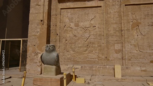 Grand courtyard of the Temple of Edfu with massive columns and monumental facade, showcasing the preserved grandeur of Ancient Egyptian architecture under clear blue sky.