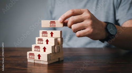 Hand stacking wooden blocks with store icons and upward arrows, representing business growth, expansion, and successful franchise development