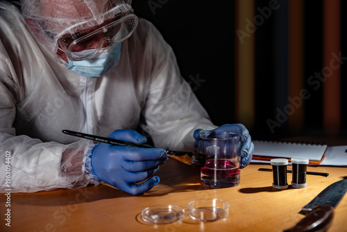 Canvas Print Crime scene evidence processing on wooden desk: gloved hands use a brush to reveal latent prints on a drinking glass beside a knife with blood stains and sample vials