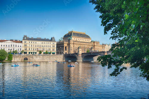 Tourists enjoying paddle boats with the National Theatre in Prague