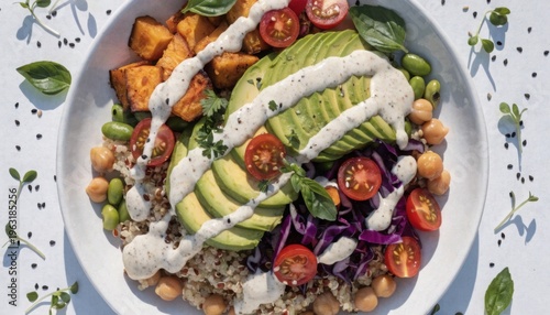Vibrant Buddha bowl with quinoa, avocado, roasted sweet potato, and fresh vegetables on white. Colorful healthy meal flat lay with natural daylight.