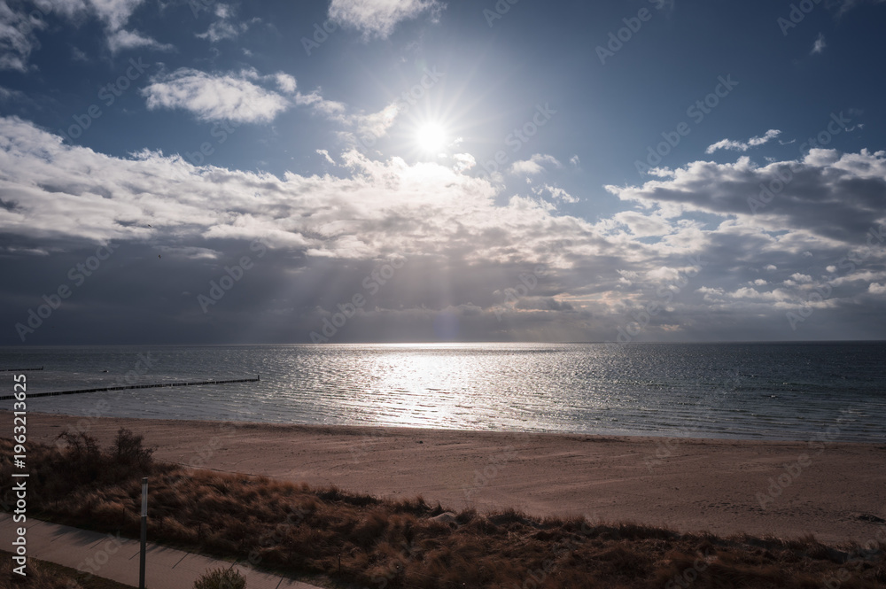 Obraz premium The sun shines through the clouds and illuminates the beach and the sea, the view over the sandy beach to the Baltic Sea, southern beach in 23775 Großenbrode, Germany