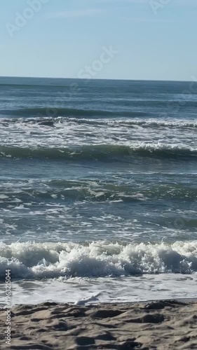 Waves gently roll onto a sandy beach, creating a calming and tranquil scene. The rhythmic movement of the ocean conveys a sense of peace and natural beauty.