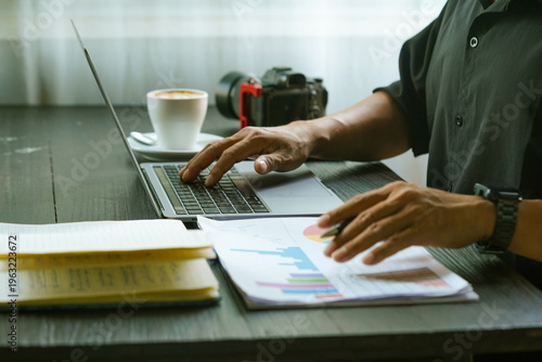 Close up of hands typing on laptop keyboard with business reports and coffee on desk.