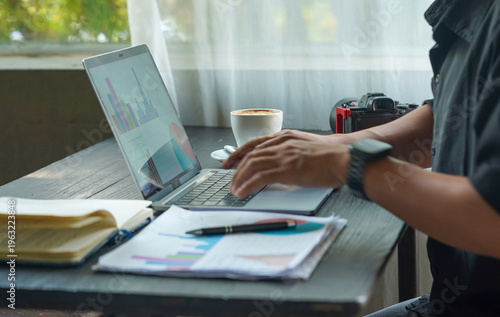 Creative workspace with laptop, camera, coffee, and business documents on wooden desk.