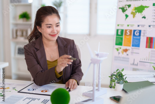 Asian adult businesswoman analyzing sustainable energy solutions discussing renewable wind power strategy at office desk with ESG data
