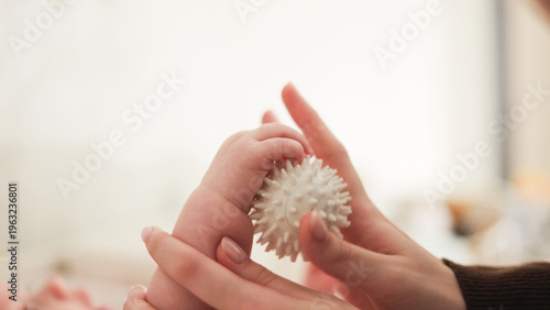 Parent's hands gently guide baby's tiny fingers around a sensory massage ball