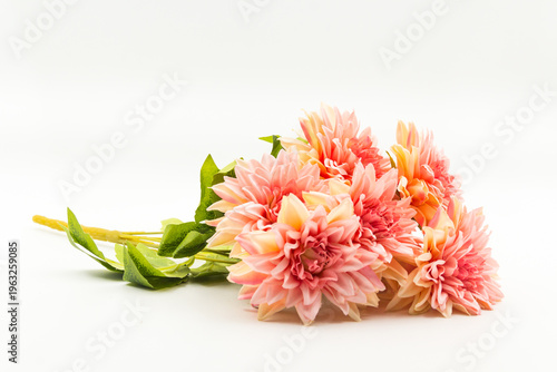 A high-quality studio shot of a vibrant artificial peach dahlia bouquet featuring multiple blooming flower heads and green leaves.
