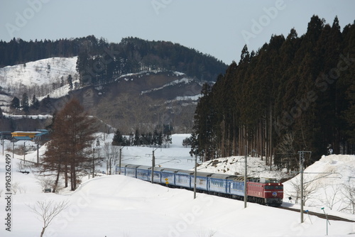 Photos 雪の積もる冬の山間部を走行する赤い電気機関車と寝台列車