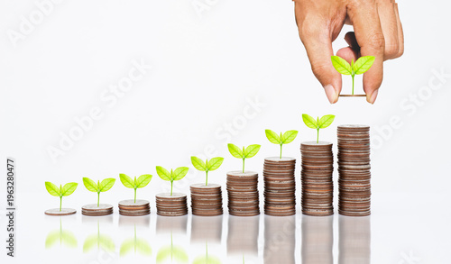 Close-up of a hand placing coins on a growing stack with green plants, representing financial growth, savings, and investment strategy. Concept wealth management, passive income, ESG business success.