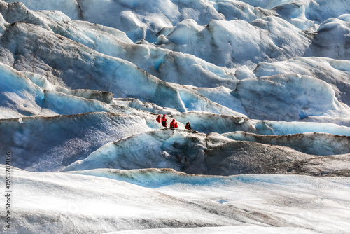 A small group of unrecognisable hikers Crossing the vast Mendenhall Glacier , Alaska