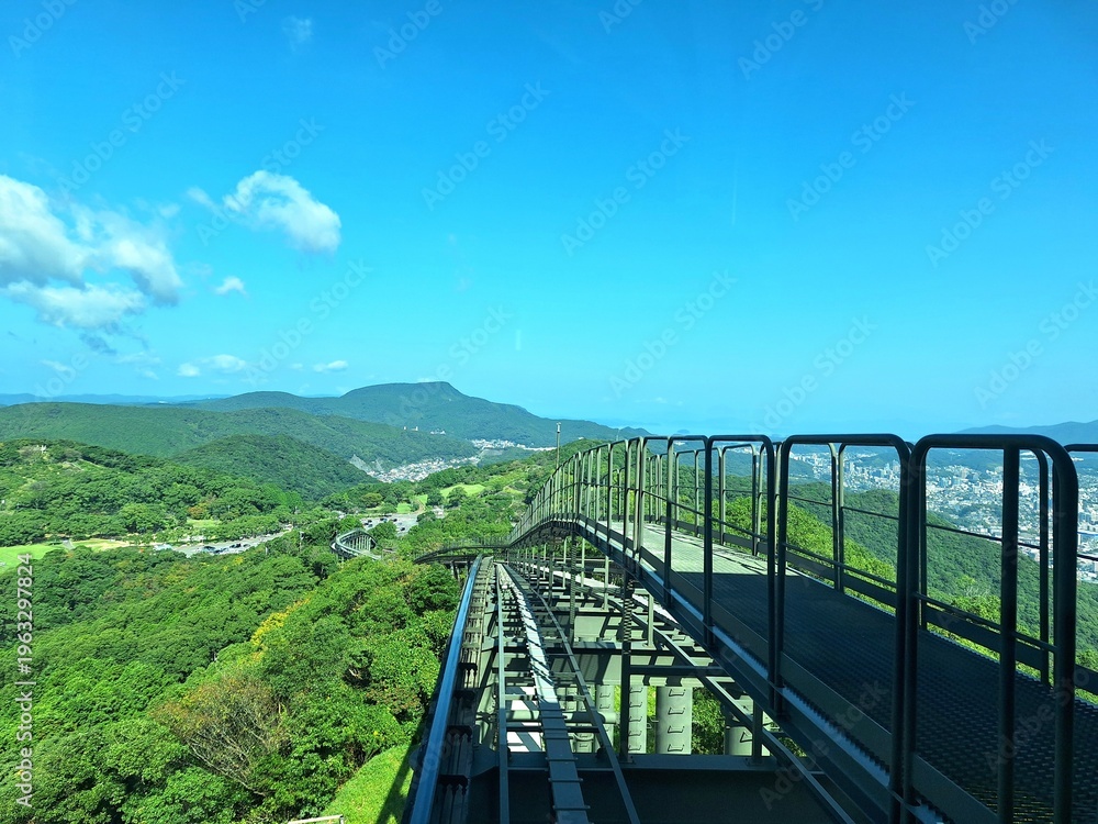 Fototapeta premium A dynamic uphill perspective from the Mount Inasa ropeway captures the sweeping green hills of Nagasaki unfolding below.