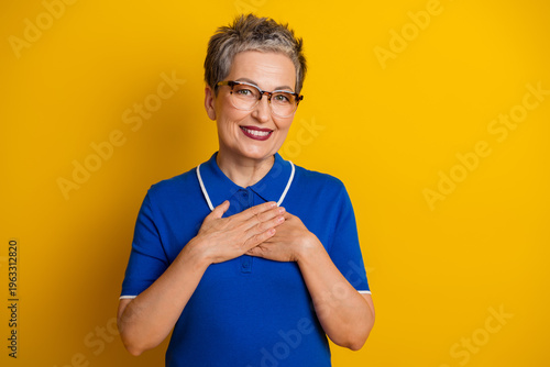 Foto A mature woman with short gray hair and glasses smiles against a bright yellow b