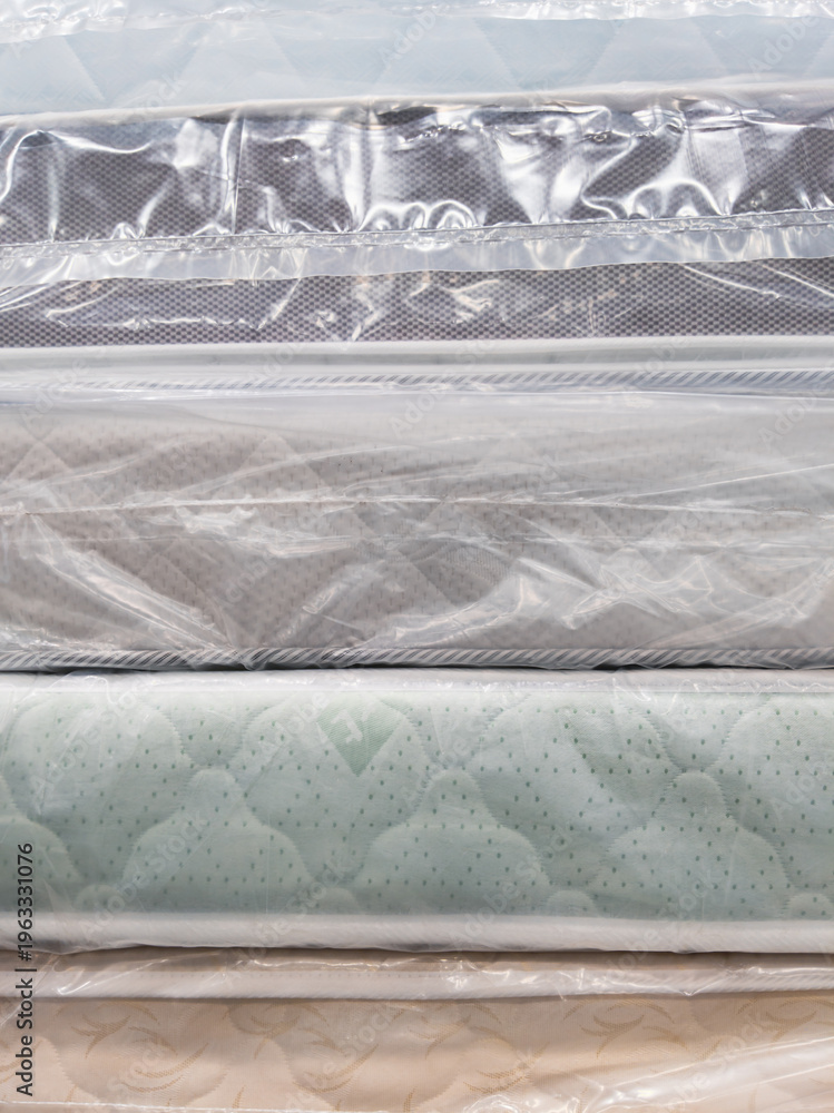 Obraz premium Stack of new mattresses in plastic wrap, various fabric covers visible from the side