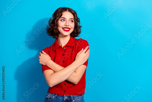 Tableau sur toile Young chic woman in red polo poses with arms crossed against blue background smi