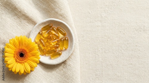 Yellow gerbera daisy and omega-3 capsules arranged on textured fabric